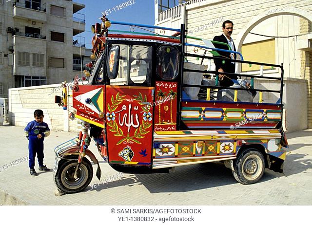 Man and his young son on a brightly painted red tricycle cart, Hama, Syria
