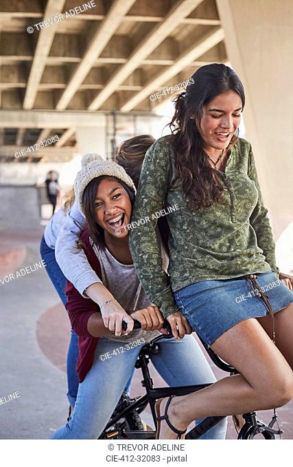 Playful teenage girls riding BMX bicycle at skate park