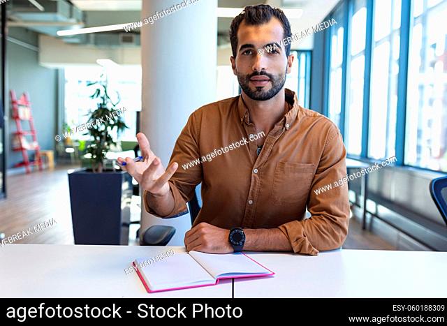 Portrait of mixed race male creative worker sitting at desk looking at camera