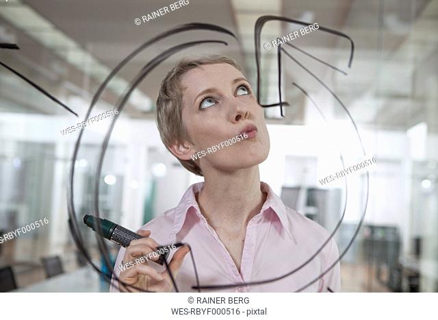 Germany, Munich, Businesswoman in office, drawing chart on glass pane