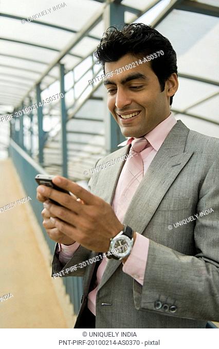 Businessman standing on a footbridge and text messaging on a mobile phone, Gurgaon, Haryana, India