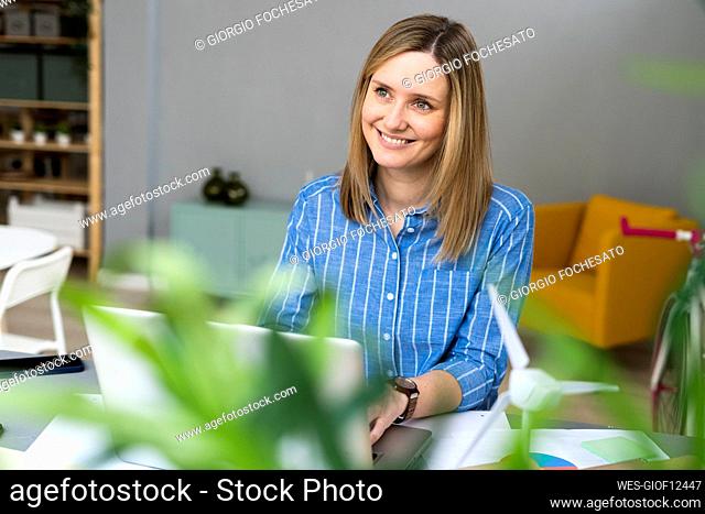 Smiling businesswoman looking away while working at desk in office