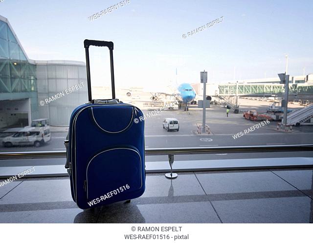 Blue suitcase at airport, airplane in background