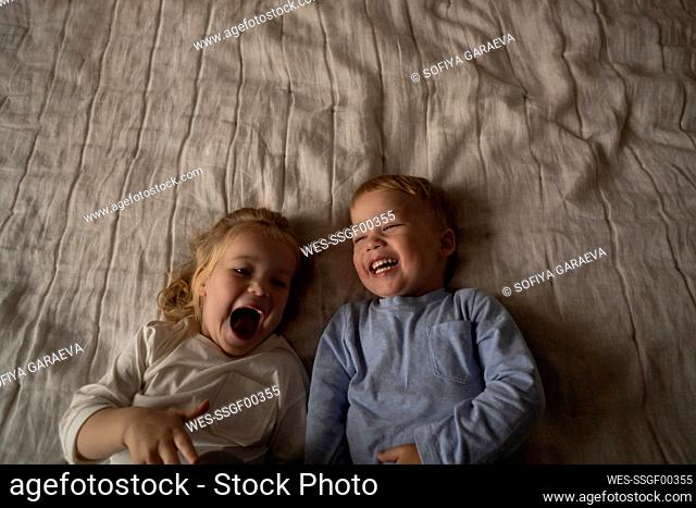 Carefree twins laughing together lying on bed at home