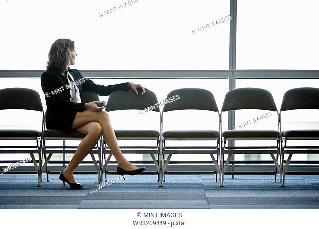 Caucasian businesswoman sitting in a row of chairs against a window in a conference centre lobby