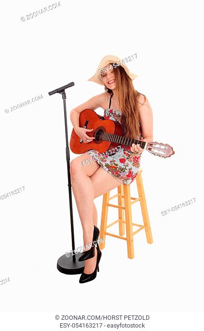 A beautiful young woman sitting in front of a microphone playing her guitar and singing, with a straw hat, isolated for white background
