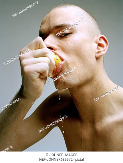 Man stripped to the waist eating a lemon