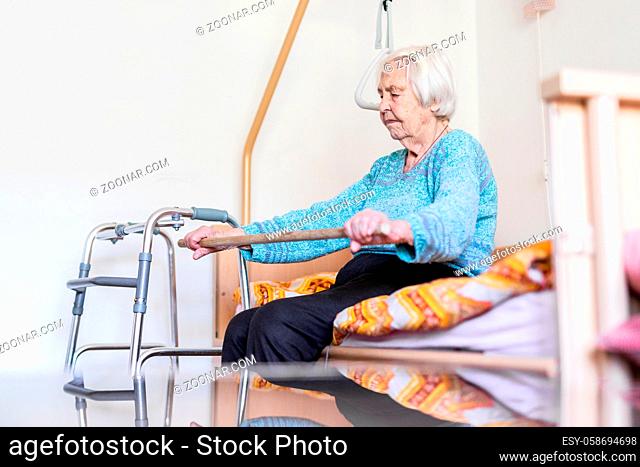 Elderly 96 years old woman exercising with a stick sitting on her bad. Geriatric health care home assisted support for older people concept