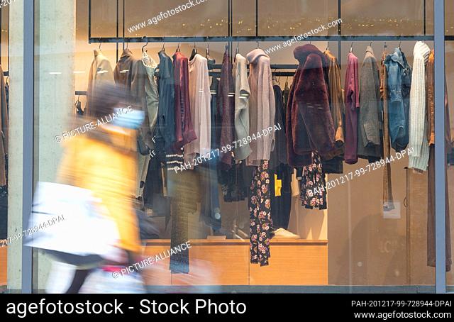17 December 2020, Baden-Wuerttemberg, Stuttgart: A woman wearing a mask walks past a closed clothing store in the Dorotheen Quartier