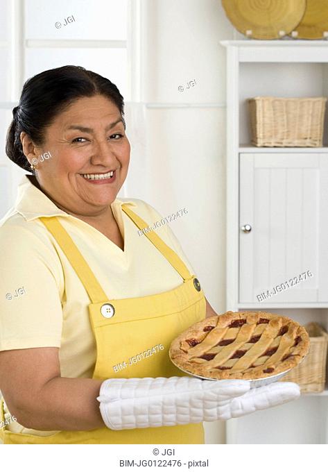 Senior Hispanic woman smiling with pie in kitchen