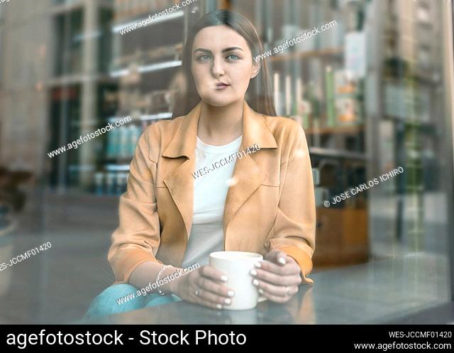 Young beautiful woman seen through glass window sitting at cafe