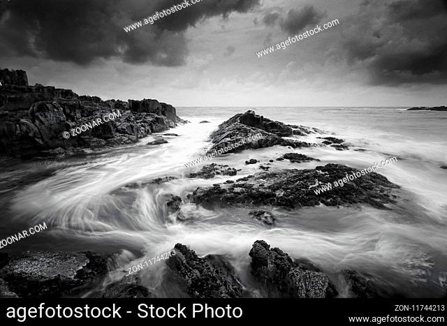 Seascape at low tide with moody clouds and pending storms and swirling ocean currents around the exposed rocks