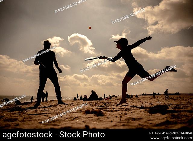 dpatop - 14 April 2022, Lower Saxony, Schillig: A father and his son play beach tennis on the North Sea beach of Schillig in beautiful weather and sunshine
