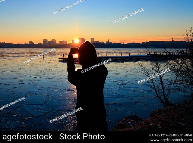 14 December 2022, Hamburg: A jogger takes a photo of the sunrise over the Alster at the Rabenstraße jetty with her smartphone