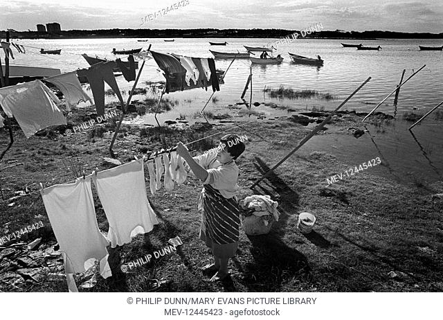A woman pegs out her washing in her tide flooded garden on the banks of the River Cavado, Portugal. first published The Sunday Times 1989