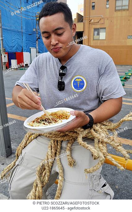 Naha, Okinawa, Japan, American soldier eating okonomiyaki in the street during the Tug of war Festival, October