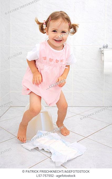 Little girl in pink dress getting up from Potty in bathroom, fooling around while doing potty training