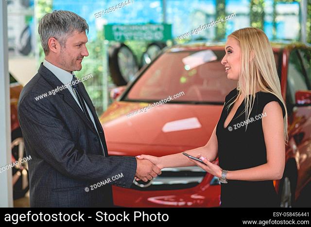 Happy young female shaking had with auto dealer. Sales manager in auto showroom shaking hand with a buyer
