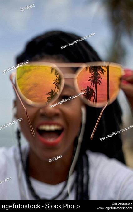 Woman showing reflection of palm trees at her mirrored sunglasses