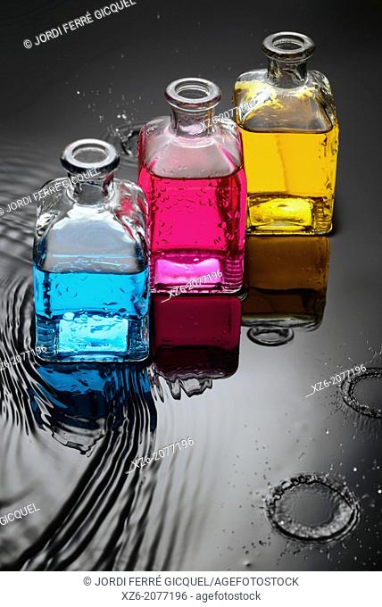 Cyan, magenta, yellow liquids in bottles on water and black background, and a close up of water droplets splashing