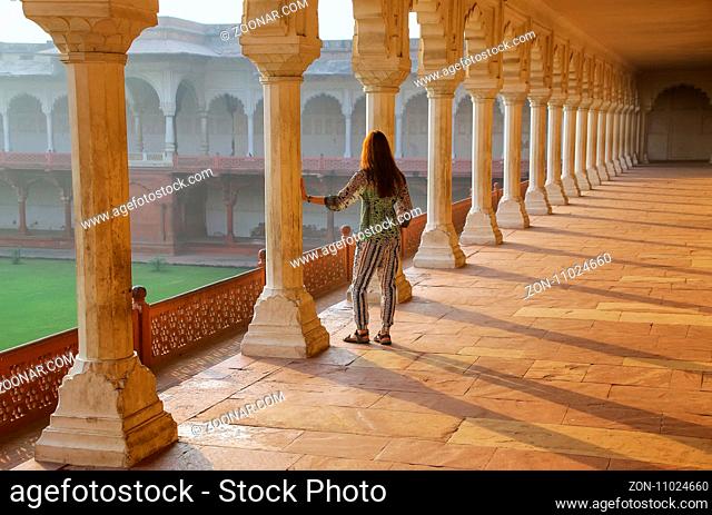Young woman standing in colonnade walkway leading to Diwan-i- Khas in Agra Fort, Uttar Pradesh, India. The fort was built primarily as a military structure