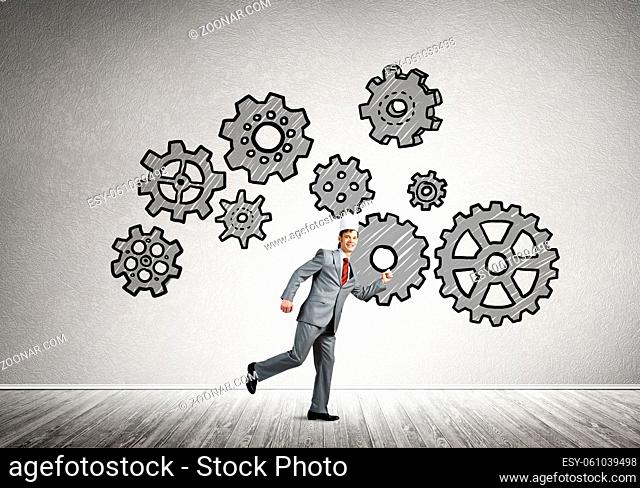 Young handsome businessman wearing white paper crown running and gear mechanism on wall