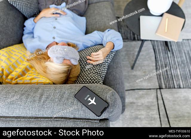 Woman wearing eye mask sleeping on sofa with smart phone at flight mode