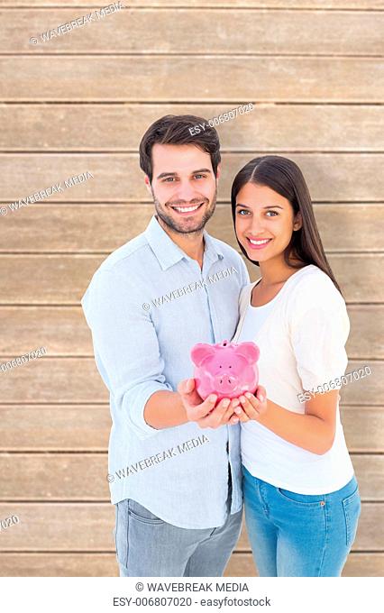 Composite image of happy couple showing their piggy bank