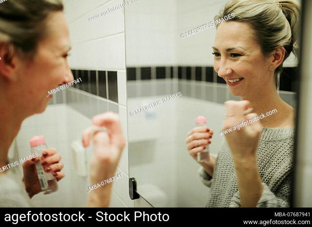 Woman in bathroom cleanses her face with facial toner
