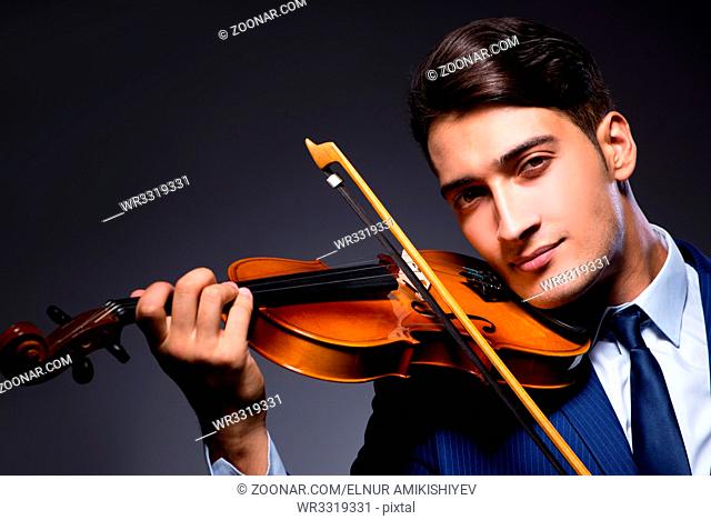 Young man playing violin in dark room