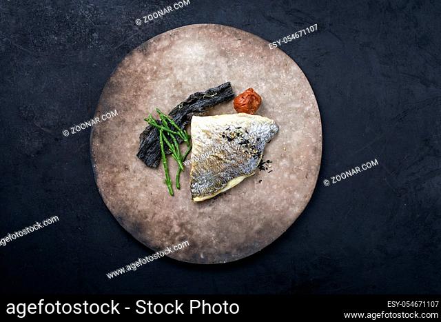 Japanese gourmet fried gilthead fish filet with glasswort, umeboshi and algae as top view on a modern design plate with copy space