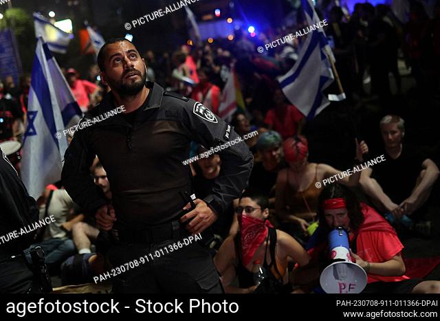 08 July 2023, Israel, Tel-aviv: An Israeli security officer stands in front of demonstrators during a protest against plans by Prime Minister Benjamin...