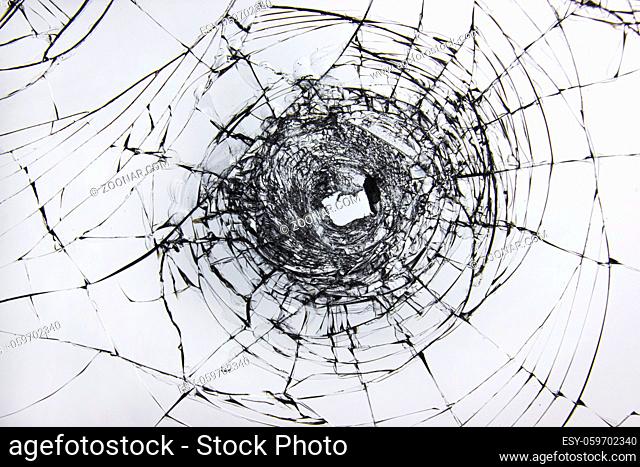 A hole and cracks in broken glass on a window of windscreen car glass. Transparent windscreen of a car with a hole after the shots