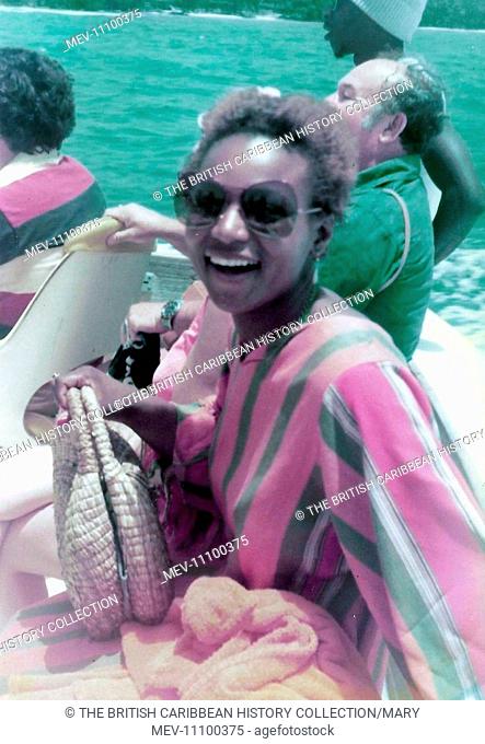 British Caribbean woman, in stripe kaftan sitting on the boat crossing the river in Ohio Rios  Jamaica. Three people in the back ground