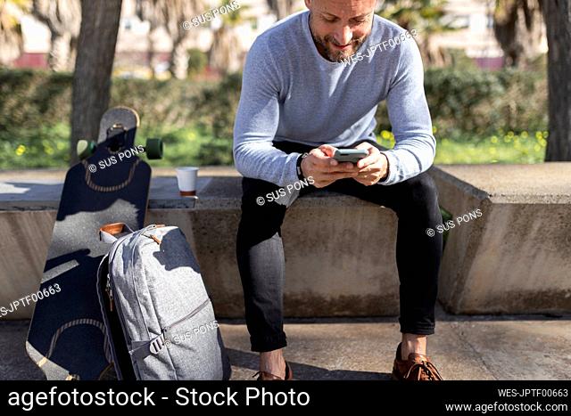 Male professional using smart phone while sitting on concrete bench at park