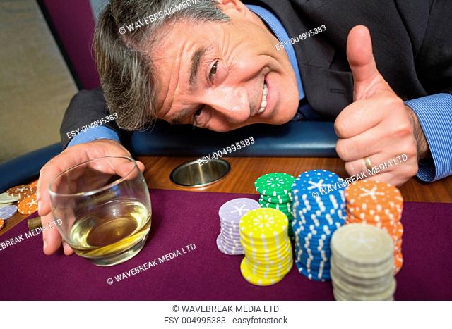 Man leaning on table with whiskey glass giving thumbs up in casino