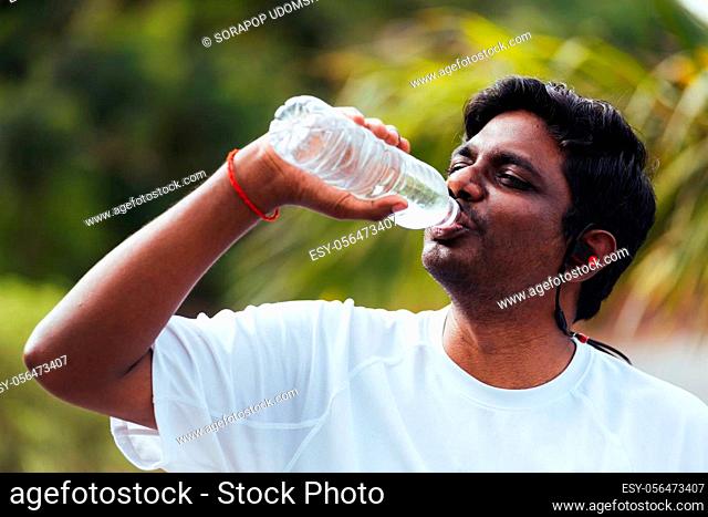 Close up Asian young sport runner black man wear athlete headphones he drinking water from a bottle after running at the outdoor street health park