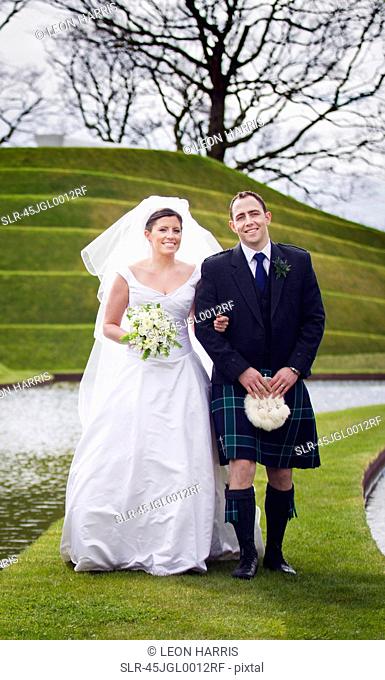 Newlywed couple walking on grassy bridge