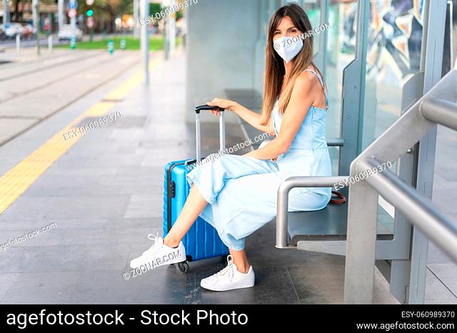 Young woman sitting at metro or tram station waiting for public transport, in medical protective mask on her face. Virus, pandemic coronavirus concept