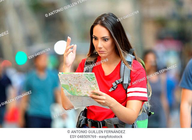 Confused teen tourist searching location in a paper guide walking on the street