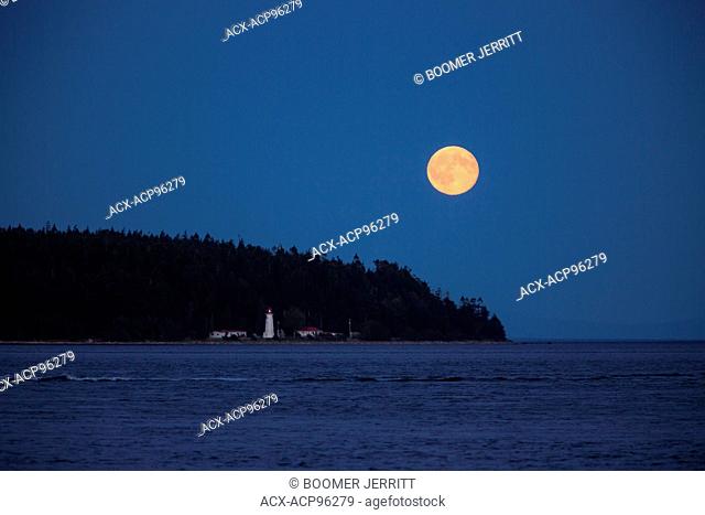 A full moon rises near the Cape Mudge lighthouse on Quadra Island. Campbell River, Vancouver Island, British Columbia, Canada