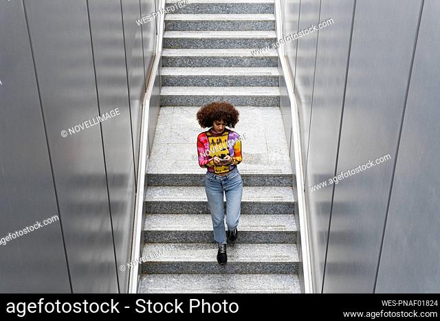 Woman using smart phone while walking on staircase