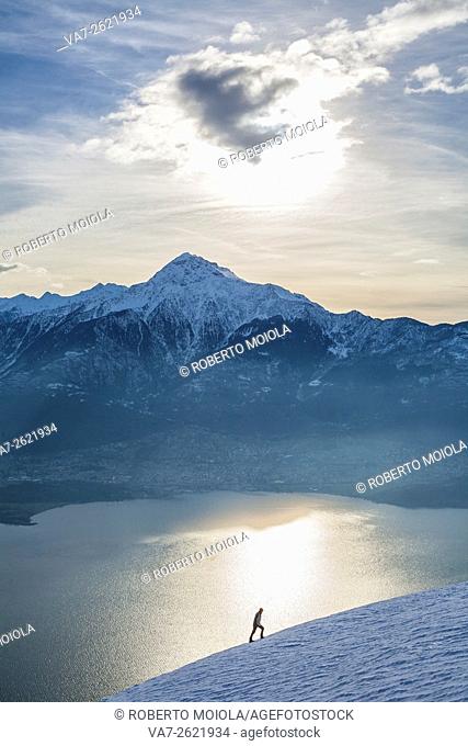 Hiker admires Lake Como and Mount Legnone on a cold winter morning Vercana mountains High Lario Lombardy Italy Europe
