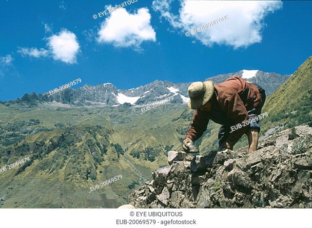 Local Quechuan man building a house, mountains in the distance