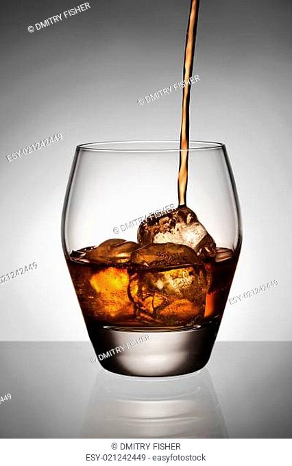 Whisky pouring on ice in glass