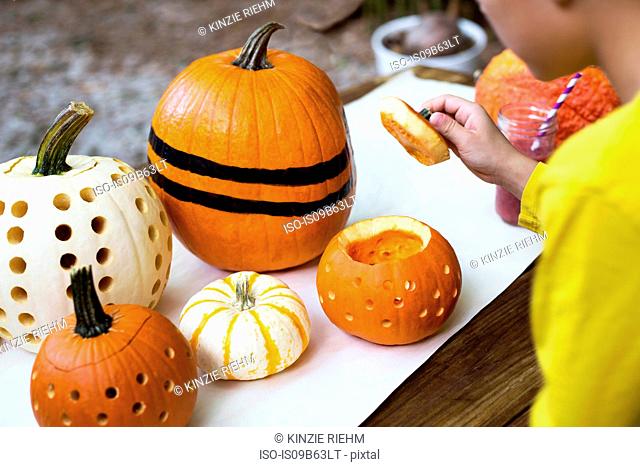 Over shoulder view of boy lifting pumpkin lid on garden table