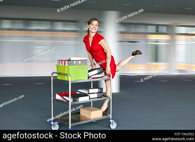 Portrait playful happy businesswoman riding office cart