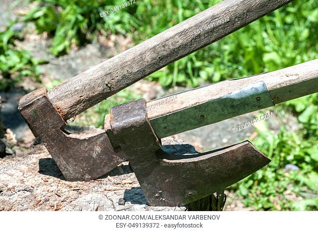 Old used weathered wooden axes stuck on wooden log for splitting wood into farmyard