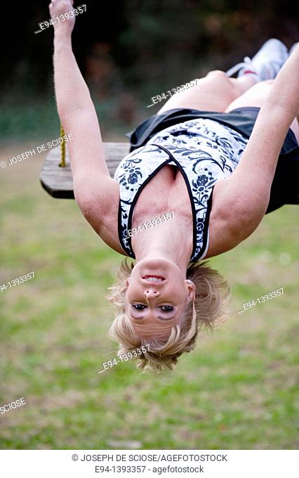 Fifty year old blond woman in fitness attire playing on a rope swing outdoors