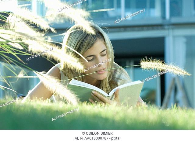 Woman lying in grass, reading book